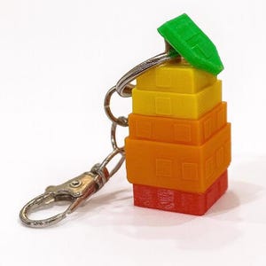 May include: A colorful keychain featuring a stack of miniature, rectangular buildings in shades of red, orange, yellow, and green. The keychain has a silver clasp and ring.