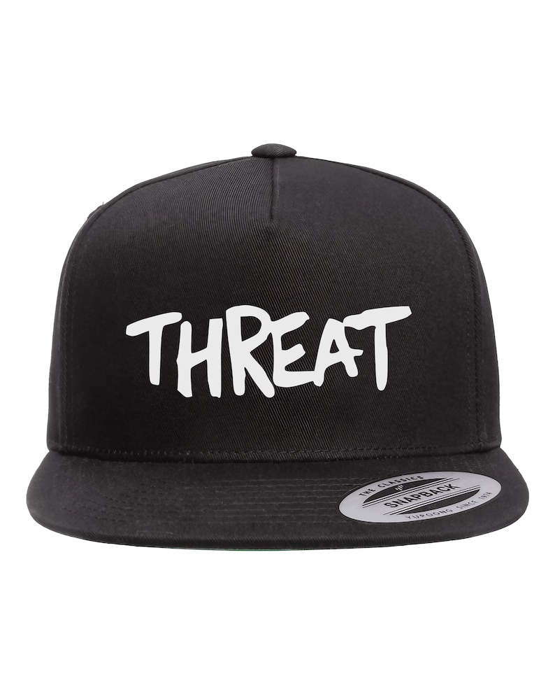 May include: Black and white baseball cap with the word "THREAT" written in white on the front. The cap has a black adjustable strap and a black snap closure.
