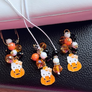 May include: Three Halloween-themed keychains with black, orange, and white beads, each featuring a small pumpkin-shaped charm with a Hello Kitty-like face.