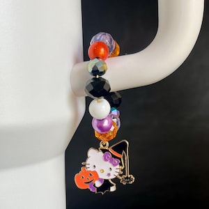 May include: A Halloween-themed charm bracelet with black, white, purple, orange, and red beads. The charm is a gold-colored Hello Kitty dressed as a witch holding a jack-o'-lantern.
