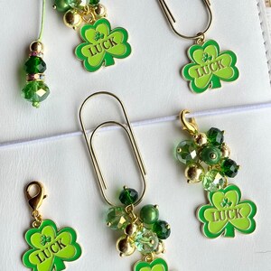 May include: A collection of St. Patrick's Day-themed accessories. Includes gold-toned paper clips and charms with green shamrock pendants. Some charms feature clusters of green beads and the word "LUCK".