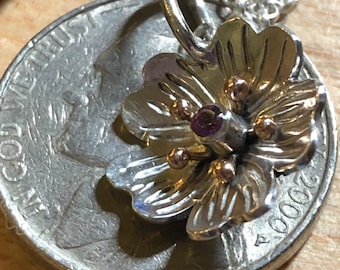 May include: A silver flower charm with a purple gemstone in the center and gold accents. The charm is about the size of a US quarter.