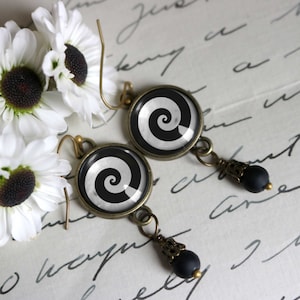 May include: A pair of black and white spiral earrings with bronze-colored metal accents and black beads. The earrings are hanging from a white surface.