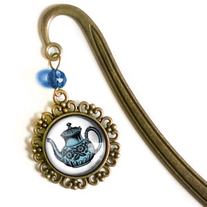 May include: A bronze bookmark with a blue and white teapot charm. The charm is in a round frame with a decorative border. The bookmark is curved and has a blue bead at the top.