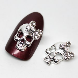 May include: Two silver skull nail charms with a rhinestone bow on top.