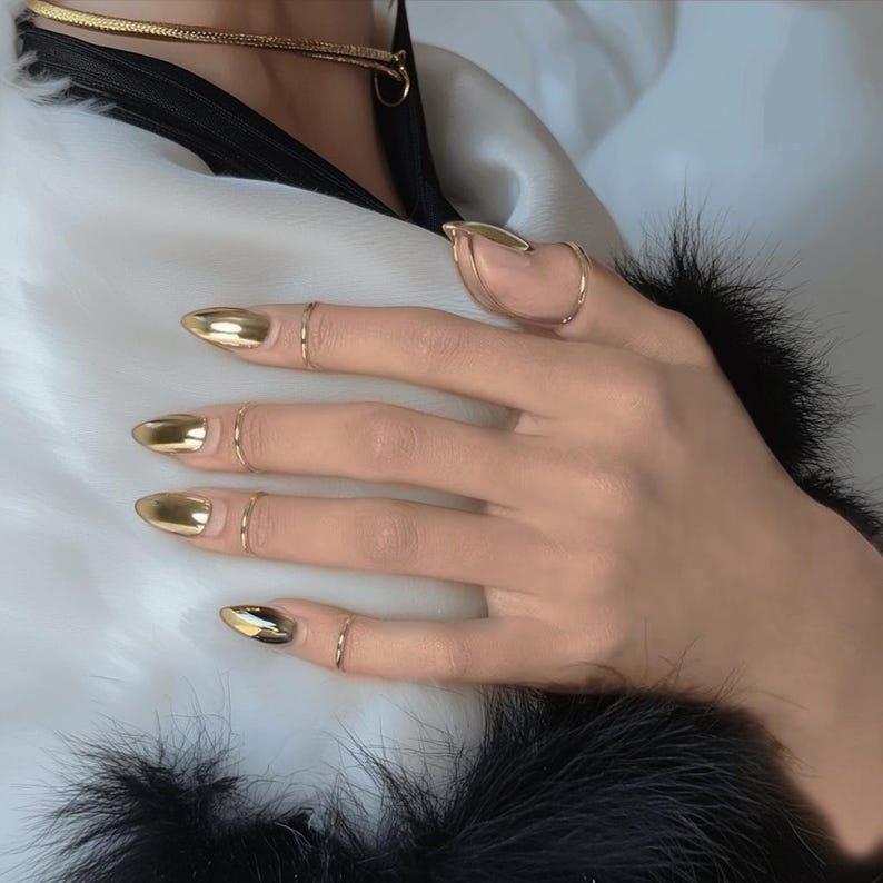 May include: A hand with gold nail polish and several gold rings on the fingers.