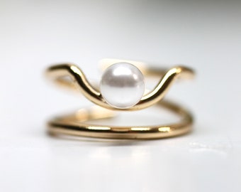 May include: A gold ring with a wave-like design and a white pearl in the center.