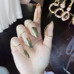 May include: Gold-toned metal finger rings with a pointed design. The rings are worn on the fingers of a hand, with the pointed ends of the rings extending beyond the fingertips.