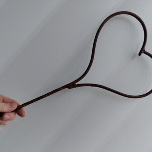 May include: A rusty metal heart-shaped object attached to a long, thin metal rod.