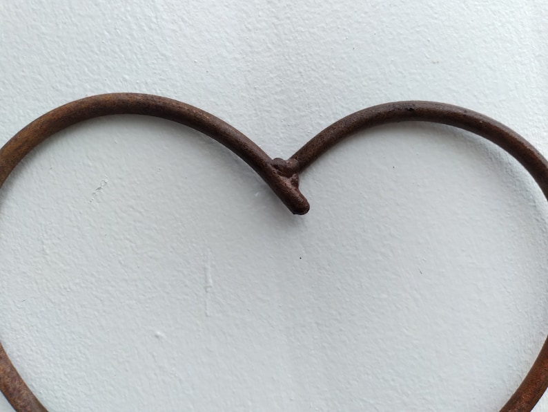 May include: A rusty metal heart-shaped frame, with a smooth, white background.