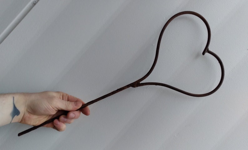 May include: A rusty metal heart-shaped object attached to a long, thin metal rod.
