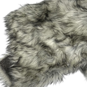 May include: Close-up of a faux fur textile with a mix of gray, black, and white fibers. The fur has a long pile and a soft, textured appearance. The material is likely used for home decor or fashion accessories.