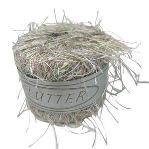 May include: A ball of yarn with a label that reads "FLUTTER". The yarn is a mix of light green, pink, and white fibers, with long, wispy strands extending from the ball. The label is a light beige color.