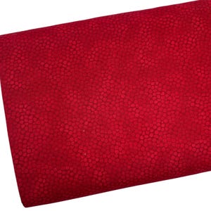 May include: A close-up of a folded piece of red fabric. The fabric has a textured surface with a pattern of small, closely spaced dots. The color is a deep, rich red.