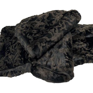 May include: A folded piece of dark brown and black faux fur fabric with a textured, curly pile. The material features a dense, wavy pattern throughout, with visible finished edges and a soft, plush appearance across the entire surface area.