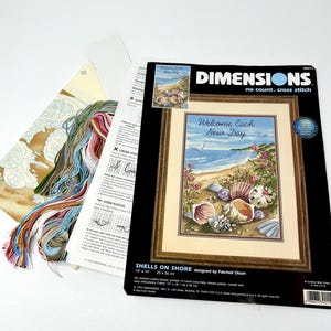 May include: A cross stitch kit featuring a beach scene with seashells and the text "Welcome Each New Day". The kit includes 14 count Aida fabric, thread palette, needle, and instructions. The kit is 10 inches by 14 inches.