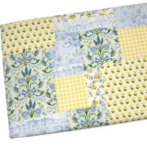 May include: A patchwork quilt featuring various patterns in yellow and blue. The quilt includes floral, gingham, and ruffled fabric sections. The color palette is soft and inviting, with a mix of botanical and geometric designs.