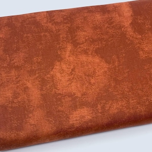 May include: A folded piece of fabric with a textured, mottled appearance. The fabric is a warm, earthy tone, with shades of rust and burnt orange. The surface has a distressed, painterly effect, suggesting a vintage or rustic aesthetic. The material appears to be a medium-weight textile.