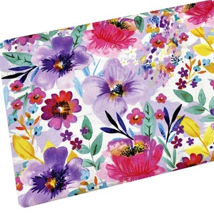 May include: A white fabric with a watercolor floral print featuring pink, purple, and yellow flowers. The fabric has a light purple background with white brushstrokes.