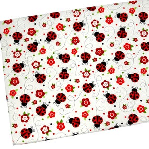May include: White fabric with a repeating pattern of red and black ladybugs, red flowers, and green leaves. The ladybugs are flying with dotted trails behind them.