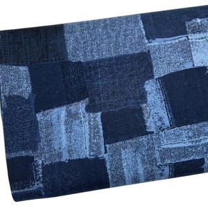 May include: A folded fabric with a patchwork design in shades of blue. The pattern features rectangular and square shapes in varying tones of denim blue, creating a textured appearance. The fabric appears to be a medium weight material.