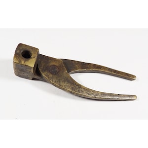 May include: Antique brass tool with a rectangular head and curved handles. The tool has a dark, aged patina, suggesting it is vintage. The handles are curved, and the head has a square hole. The tool is likely used for a specific mechanical purpose.