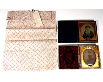 May include: An assortment of antique photographs in ornate frames, alongside a floral patterned fabric pouch with a tag. The photographs feature portraits of individuals, with one framed in gold and another in a dark frame.