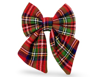 May include: A large, fabric bow in a classic plaid pattern. The bow features a combination of red, green, brown, and yellow colors. The bow is a festive accessory, suitable for various occasions.