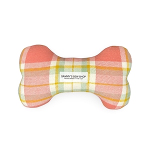 May include: Bone-shaped dog toy with a plaid pattern in shades of pink, yellow, and green. The toy has a white label that reads "SAMMY'S SEW SHOP Handcrafted In The USA".