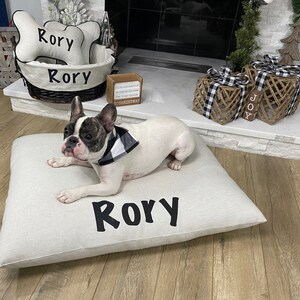 Frenchie lay a top of a luxury pillow bed, personalized with his name sitting by a fireplace with a wicker basket for his toys.