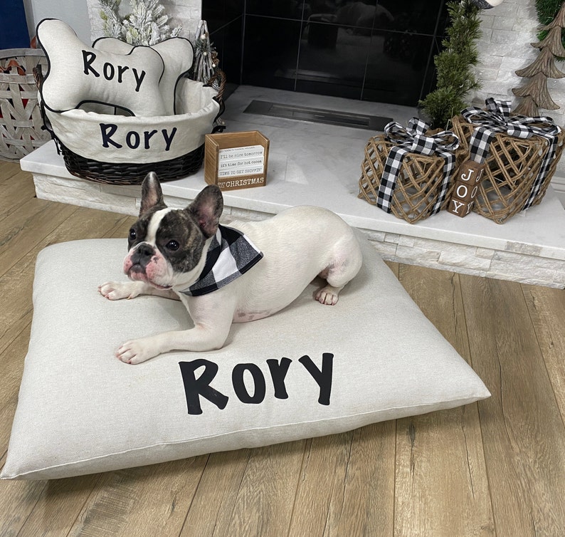 Frenchie lay a top of a luxury pillow bed, personalized with his name sitting by a fireplace with a wicker basket for his toys.