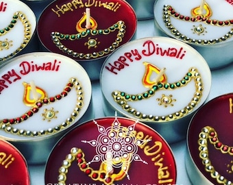 May include: A collection of round tea light candles in white and deep red wax. Each candle features a hand-painted diya lamp design decorated with small metallic beads and the handwritten text Happy Diwali in red or gold paint on the surface.