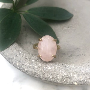 May include: A gold ring with a large oval-shaped rose quartz gemstone.