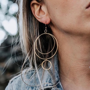 May include: Gold double hoop earrings with a smaller circle dangling from the bottom.