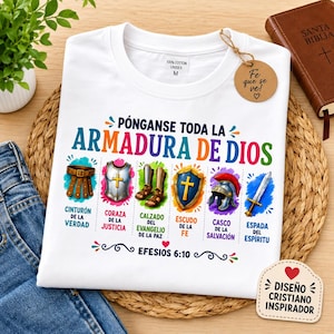 May include: A white t-shirt featuring a colorful graphic of the Armor of God with Spanish text including Pónganse toda la armadura de Dios and Efesios 6:10. The design displays illustrations of a belt, breastplate, sandals, shield, helmet, and sword.