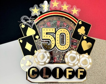 May include: A black and gold casino-themed cake topper with the number 50, a roulette wheel, playing cards, and the name "CLIFF".