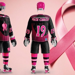 Puede incluir: Una camiseta de hockey negra con detalles rosas y un dise&ntilde;o de cinta rosa. La camiseta tiene el texto "Puck Cancer" y el n&uacute;mero "19" en la parte delantera. La camiseta la lleva un jugador de hockey con un casco rosa y guantes rosas.