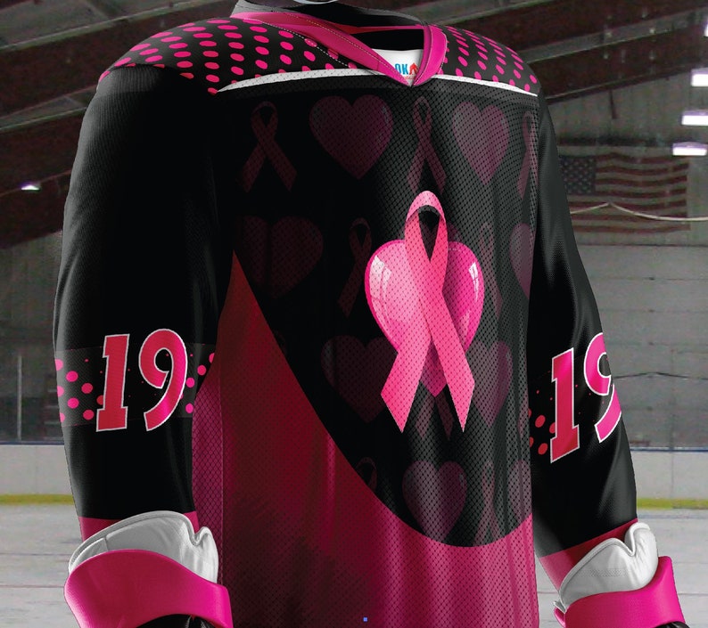 Puede incluir: Camiseta de hockey negra con corazones y cintas rosas. La camiseta tiene el n&uacute;mero 19 en ambas mangas.