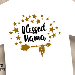 Puede incluir: Camiseta blanca con un diseño de flecha dorada y estrellas. El texto "Blessed Mama" está escrito en negro.