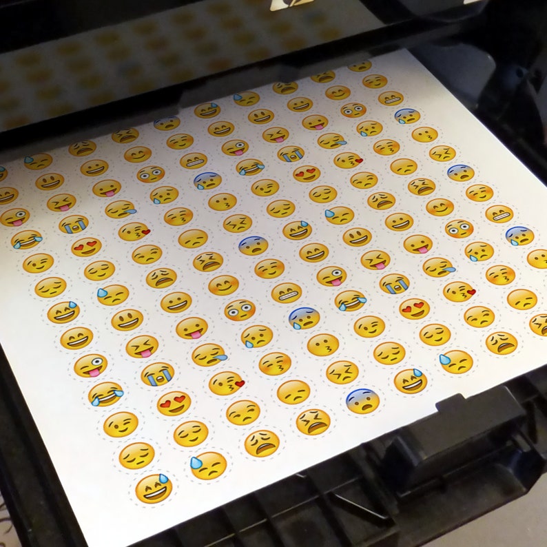 May include: A sheet of paper with a grid of yellow emoji stickers printed on it. The emojis are all different facial expressions, including happy, sad, surprised, and angry.