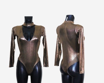 May include: A gold metallic long-sleeved bodysuit with a high neckline and a plunging V-neck. The bodysuit has a fitted silhouette and a snap closure at the crotch.