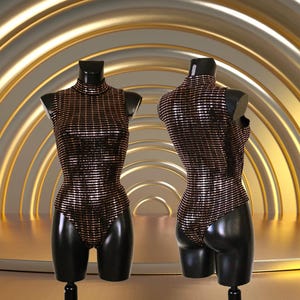 May include: Two black mannequins display a shimmering, high-neck bodysuit. The bodysuit is covered in horizontal stripes of copper-colored sequins. The mannequins are set against a gold and cream-colored backdrop.