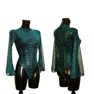 May include: A teal bodysuit with long sleeves and a high neckline. The fabric has a shimmering, dotted pattern. The sleeves flare out from the elbow. The bodysuit is displayed on a black mannequin.