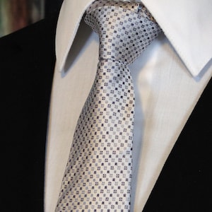 May include: A light gray patterned tie with a white background. The tie has a small, repeating pattern of squares.