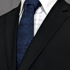 May include: A black suit jacket with a dark blue paisley patterned tie featuring a skull design. The tie is worn with a white dress shirt.