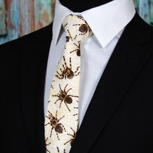 May include: A white tie with a pattern of brown spiders and webs. The tie is worn with a white dress shirt and a black suit jacket.