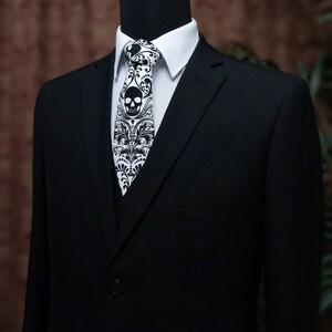 May include: A black suit jacket with a white collared shirt and a black and white skull patterned tie.