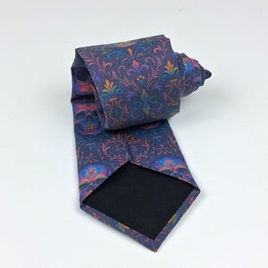 May include: A rolled-up necktie with a dark blue background and a repeating pattern of skulls and floral designs in shades of purple, orange, and blue. The tie has a black backing.