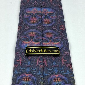 May include: A dark blue necktie with a repeating pattern of colourful skulls and floral designs. The tie has a black label with the text "EdsNeckties.com" in gold lettering. The tie is made of a smooth fabric.