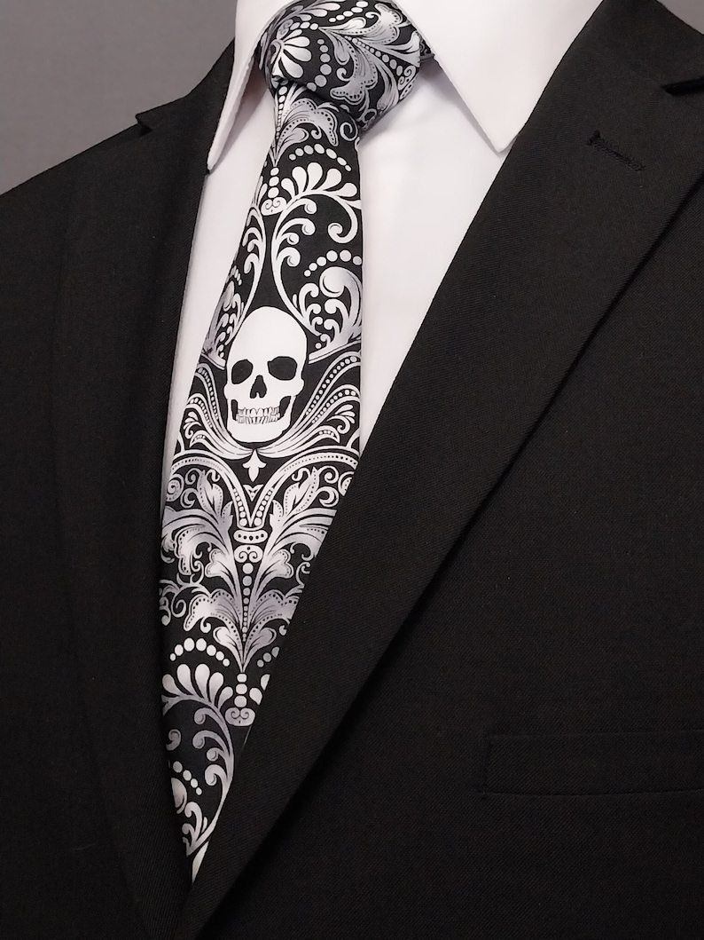 May include: A black and white patterned tie with a white skull design. The tie is made of silk and has a satin finish.
